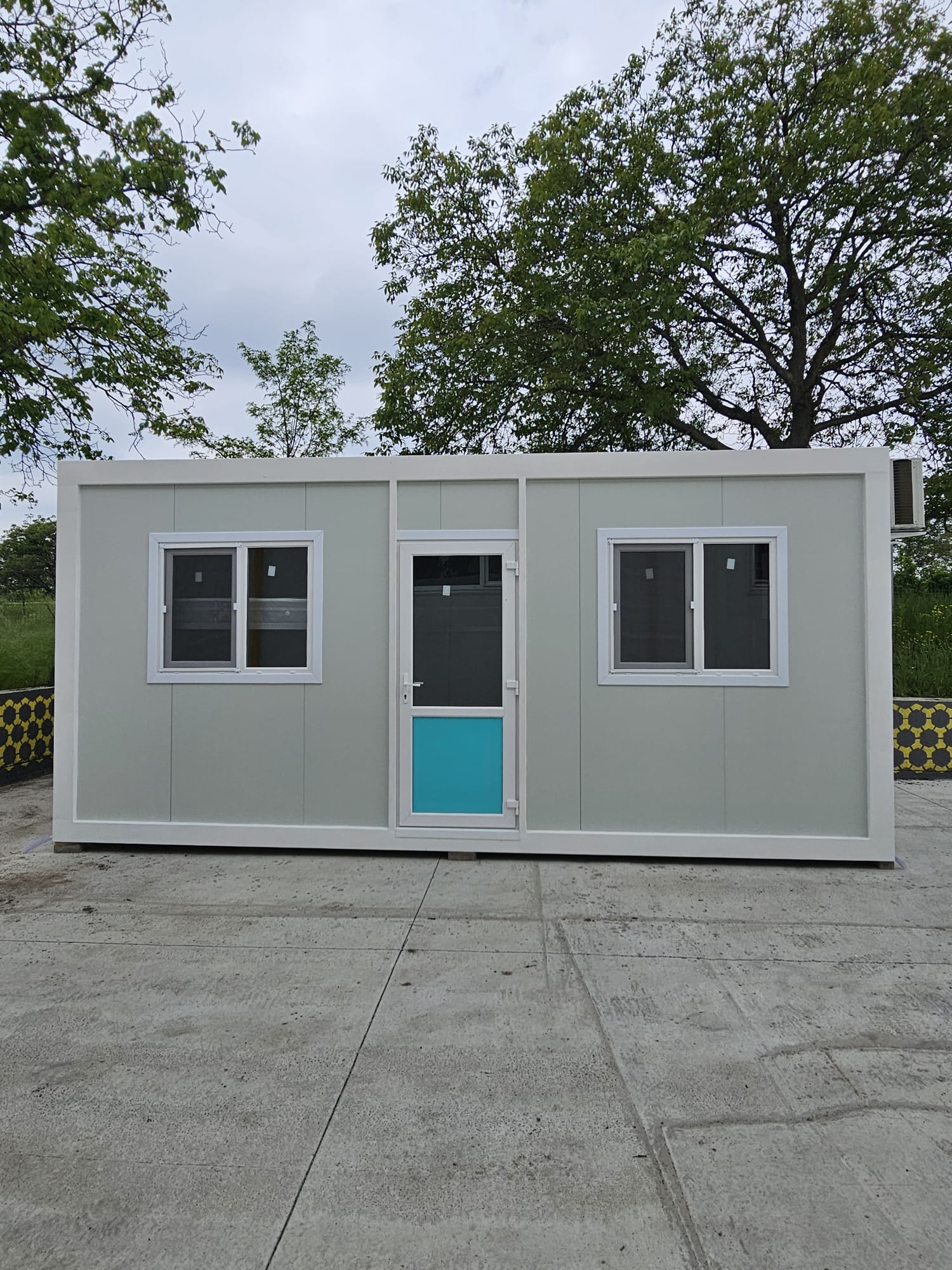 Container modular locuibil gri deschis cu două ferestre și ușă centrală